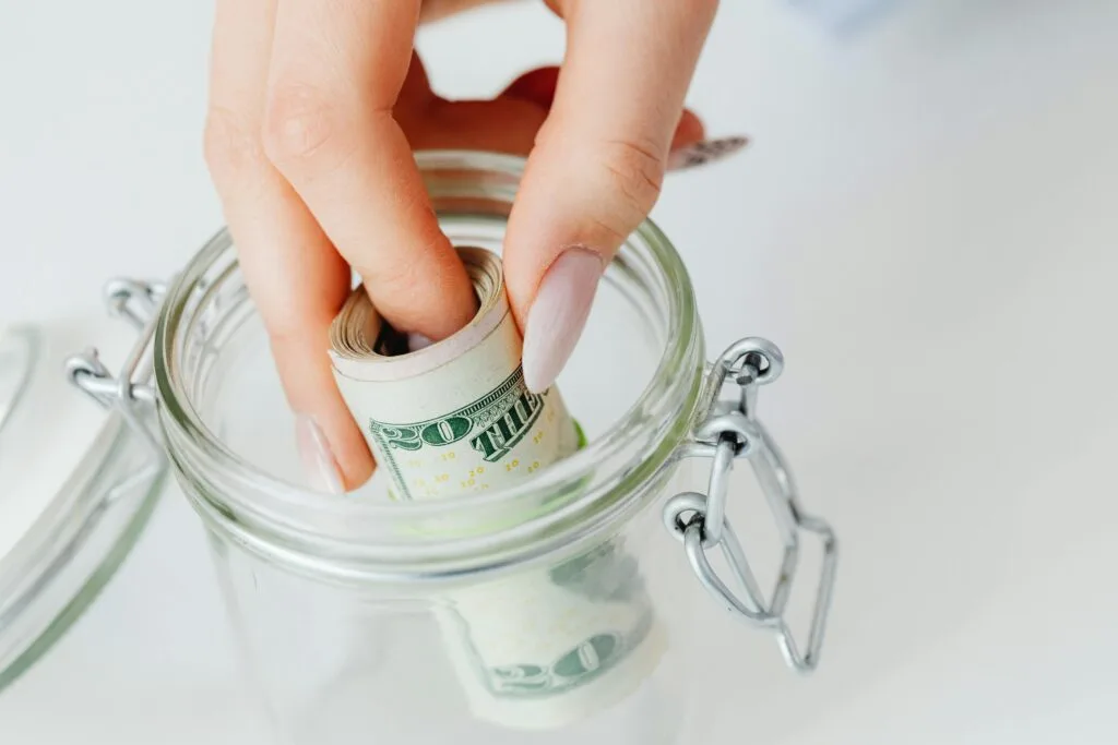 Woman putting cash in glass jar for emergency fund