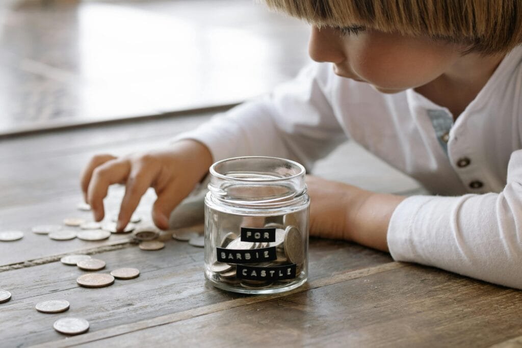 Child counting money with jar of coins that has "for barbie castle" written on the side