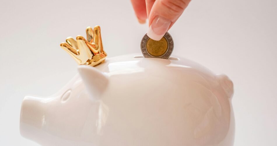 Woman's hand putting money in white piggy bank with crown on it to visualize saving for retirement in your 30s